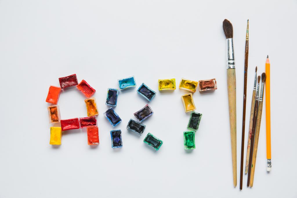 Top uitzicht op verfborstels, potlood en kunst belettering gemaakt van verven op witte achtergrond - Foto, afbeelding