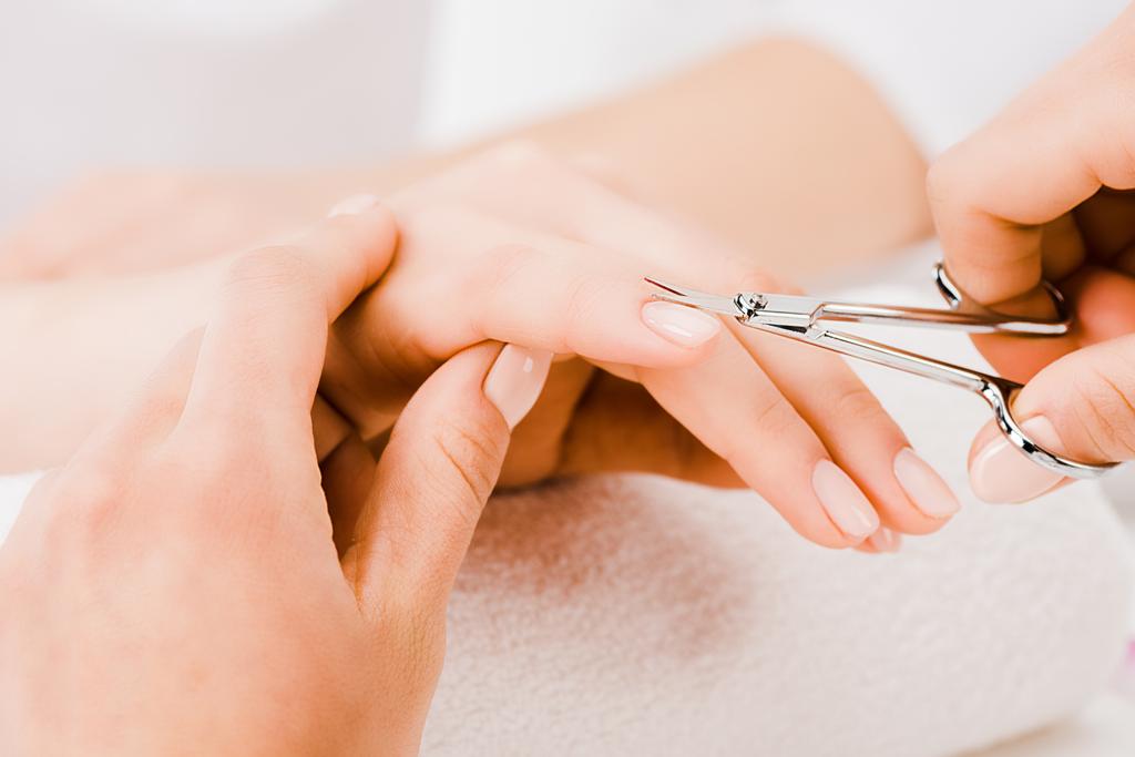 Cropped view of manicurist gently holding hand while cutting cuticle - Photo, Image
