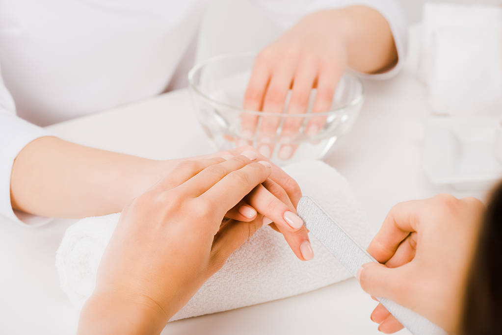 Vista parcial da manicure segurando a mão feminina e usando o arquivo de unhas
  - Foto, Imagem
