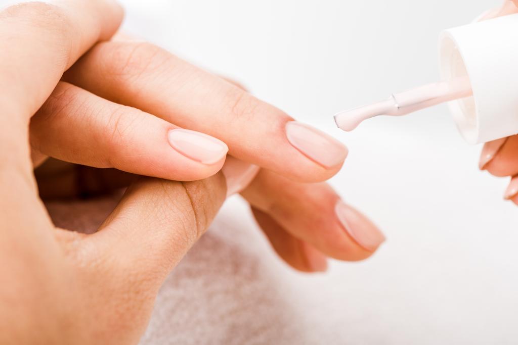 Обрезанный вид маникюра, держащегося за руку и наносящего лак на ногти
  - Фото, изображение