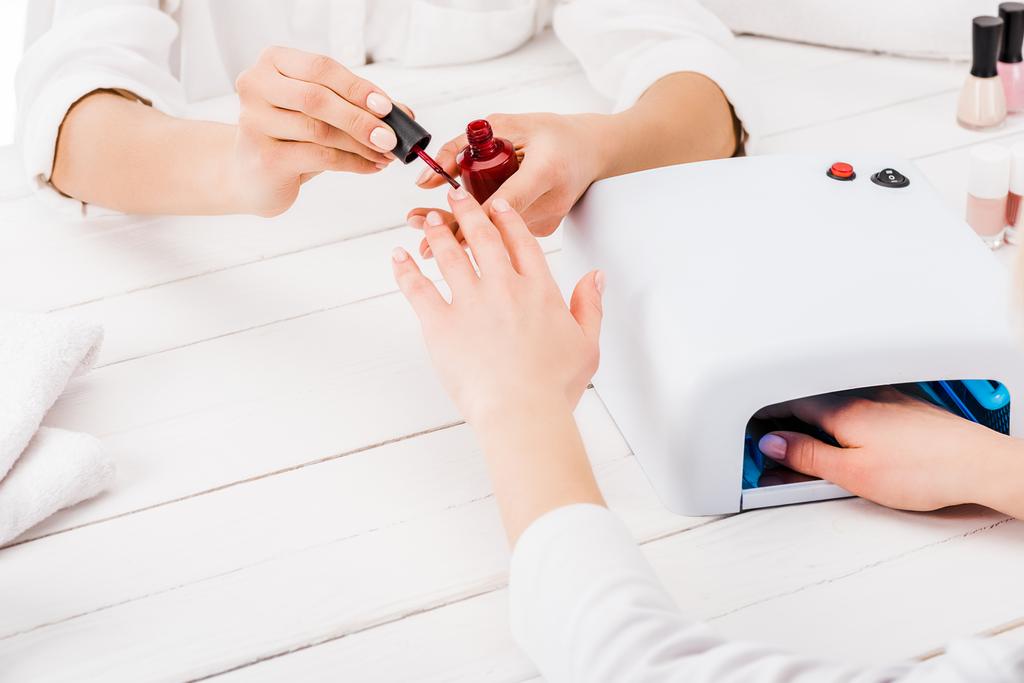 Partial view of woman dries nail polish while manicurist painting fingers in red - Photo, Image