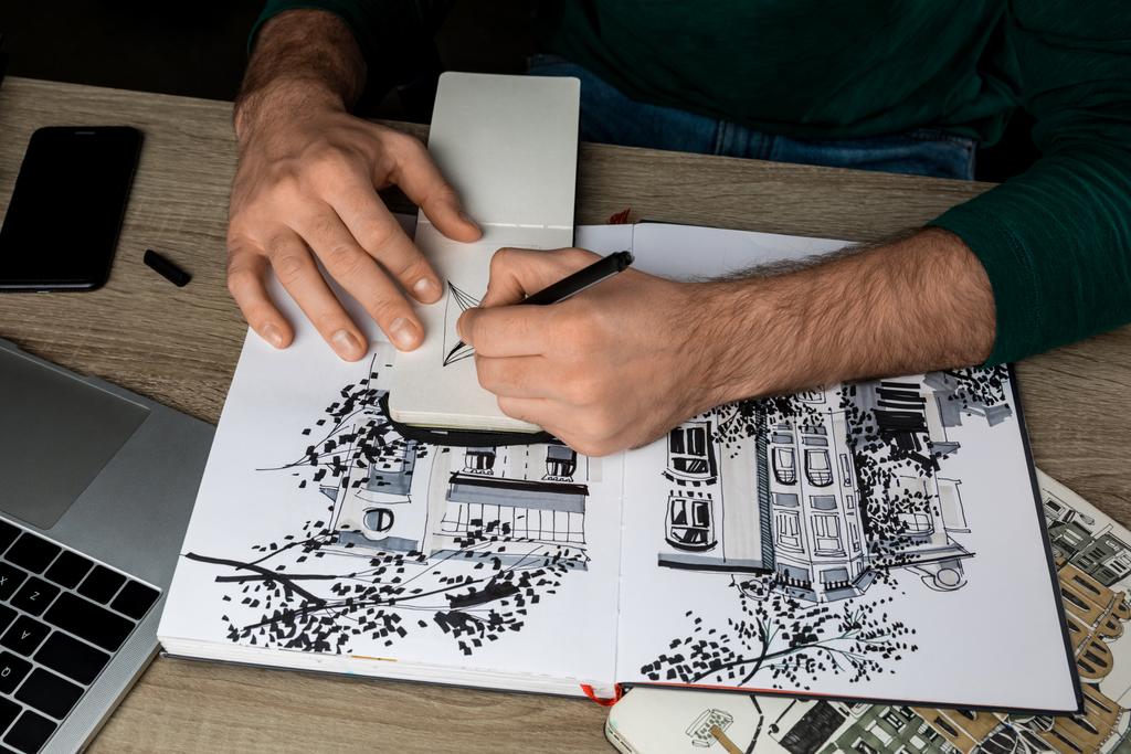 vista superior do homem mãos desenho em notebook na mesa de madeira ao lado de álbuns e gadgets
 - Foto, Imagem