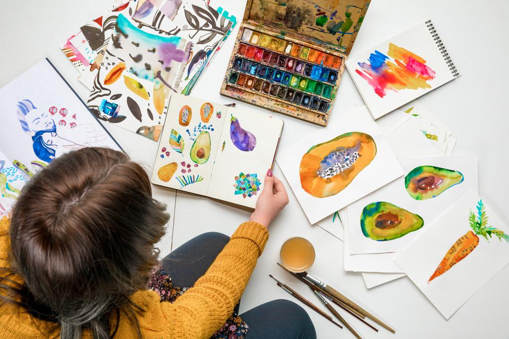 vista superior de la mujer sentada rodeada de dibujos a color y utensilios de dibujo
 - Foto, imagen