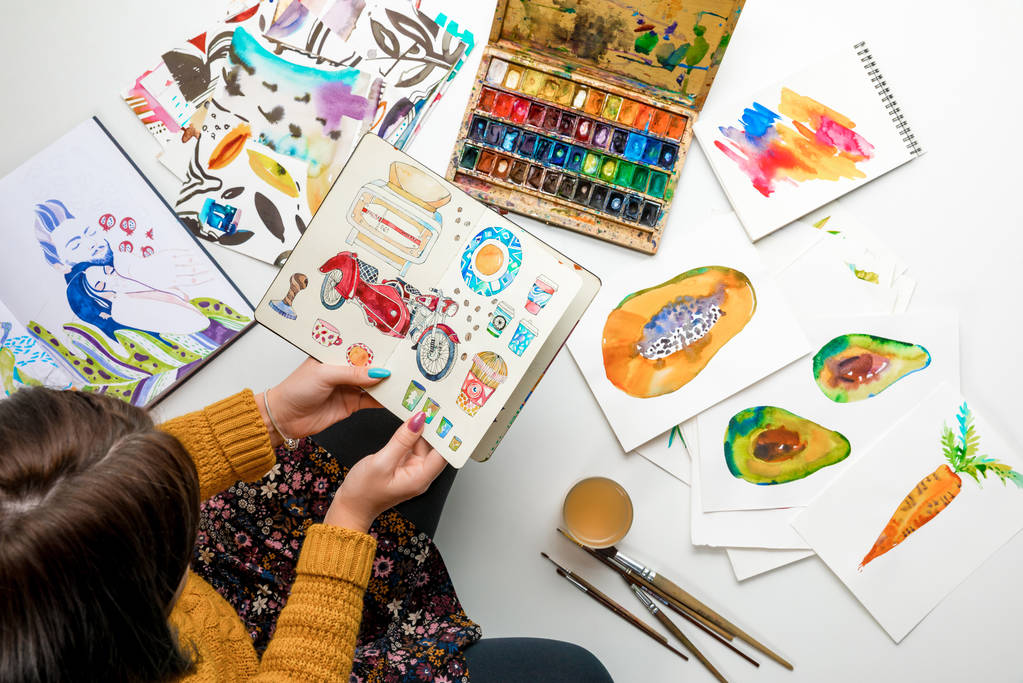 top view of woman holding album surrounded by color drawings and drawing utensils - Photo, Image