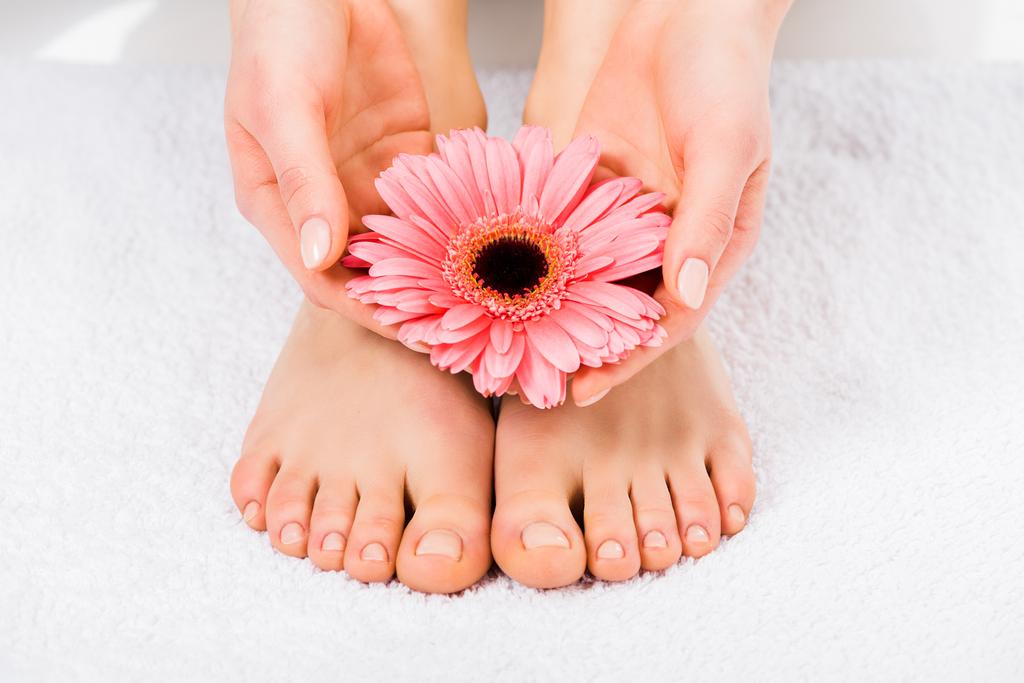 Vista parcial de una mujer descalza de pie sobre una toalla y sosteniendo una flor
 - Foto, imagen