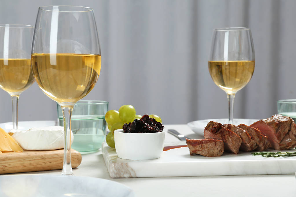 Gustose bistecche e bicchieri di vino bianco serviti in tavola
 - Foto, immagini