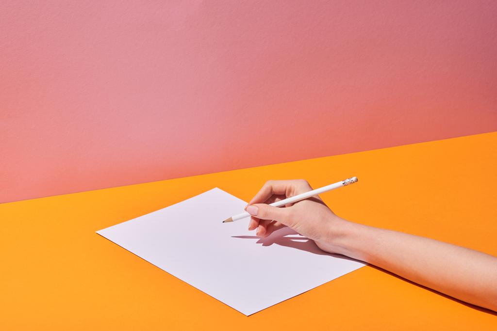 cropped view of woman writing on paper on yellow desk and pink background - Photo, Image