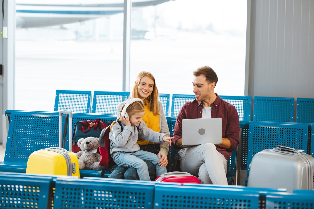 чарівна дочка вказує пальцем на ноутбук, сидячи поруч з татом і мамою в аеропорту
  - Фото, зображення