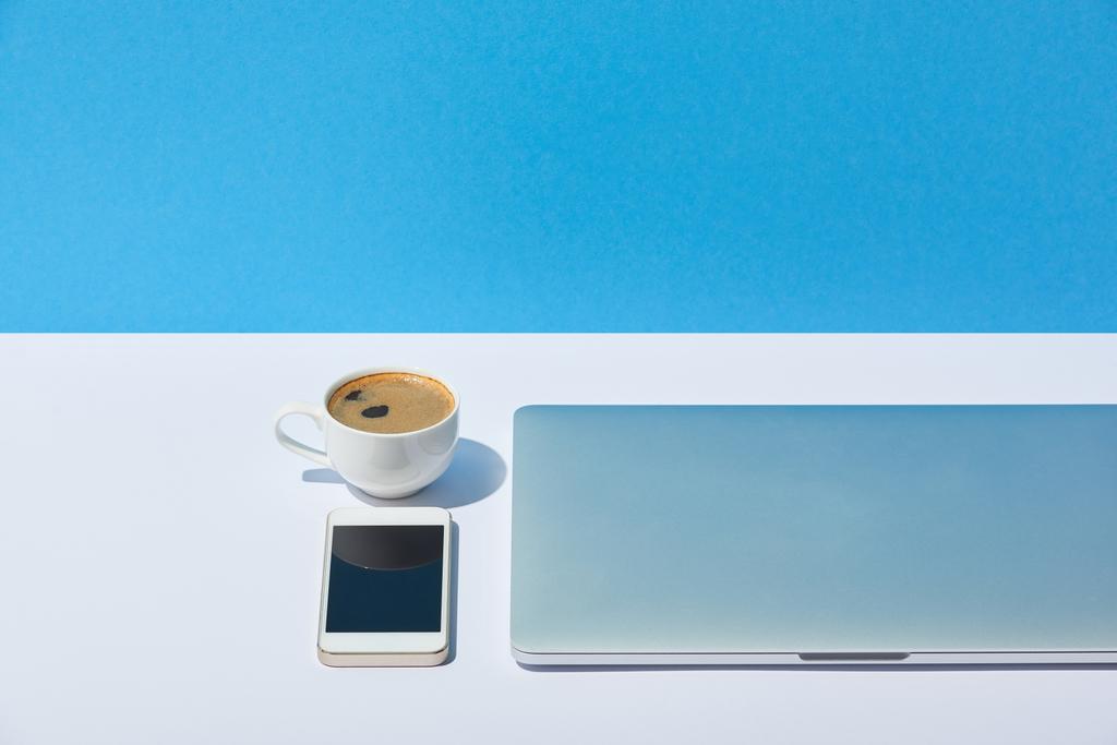 白い机と青色の背景にスマート フォンやノート パソコン、コーヒー カップ - 写真・画像
