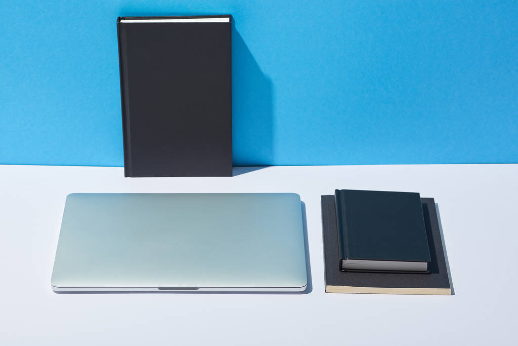 laptop and notebooks on white desk and blue background - Photo, Image