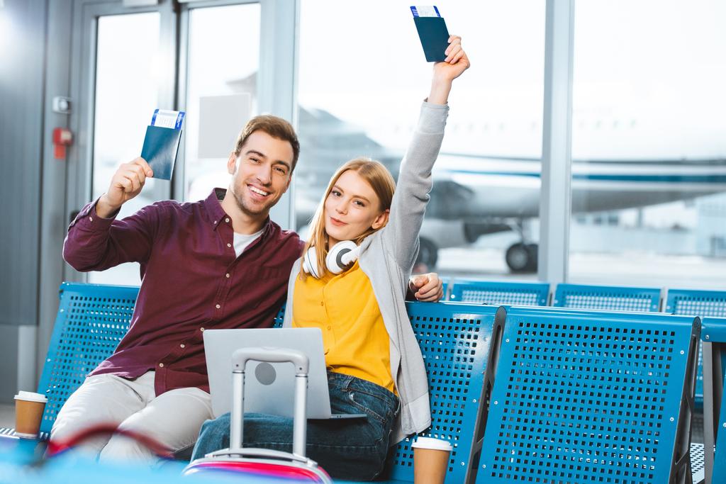 happy girlfriend holding passport above head near smiling boyfriend in airport near luggage  - Photo, Image