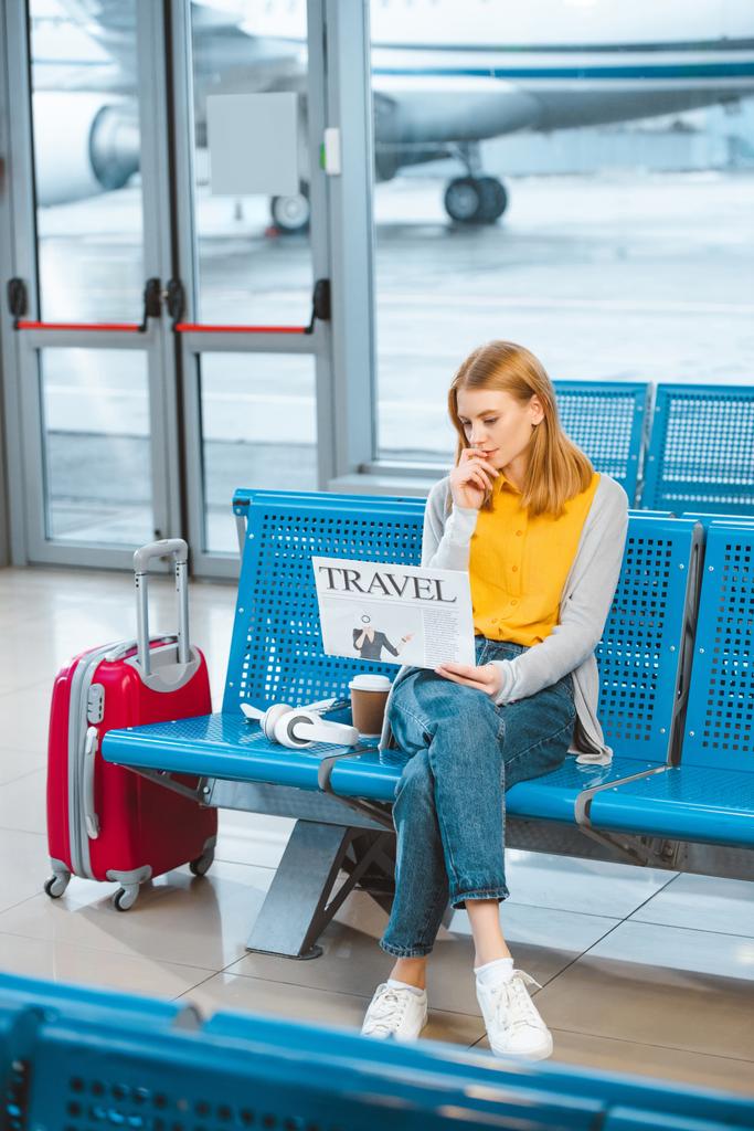 atractiva mujer leyendo periódico de viaje cerca de la maleta en el aeropuerto
  - Foto, imagen