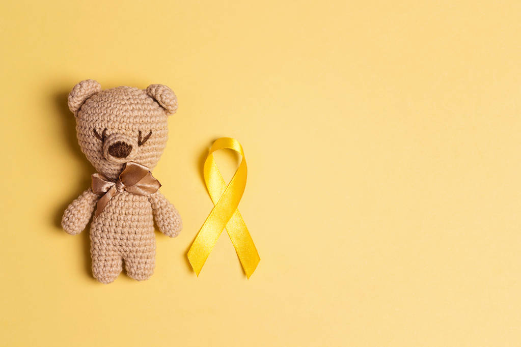 Kinder speelgoed met een Childhood Cancer Awareness Yellow Ribbon op gele achtergrond. Childhood Cancer dag 15 februari,. - Foto, afbeelding