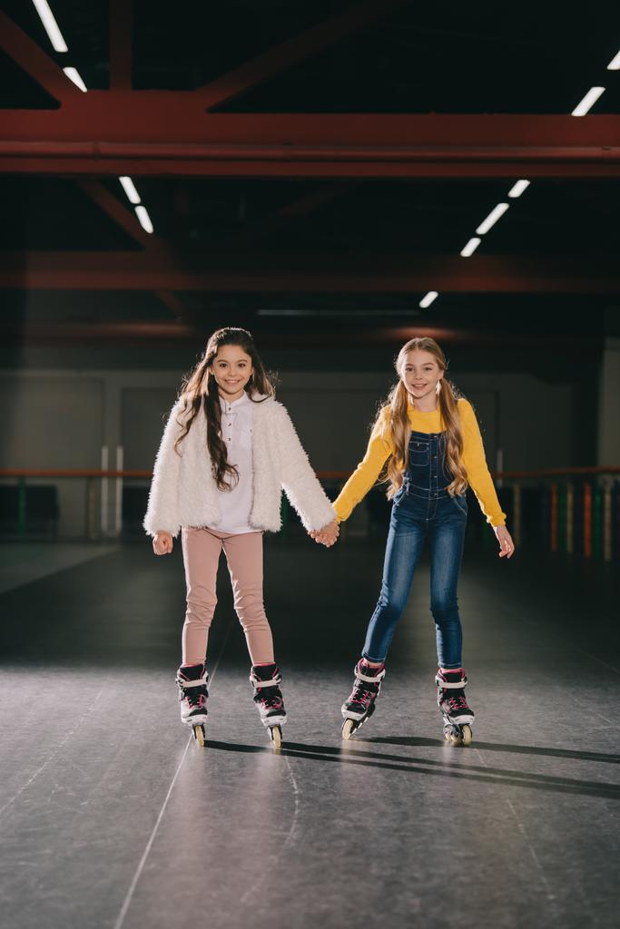 Dos lindos niños de pelo largo en patines de pie en pista de patinaje y tomados de la mano
 - Foto, imagen