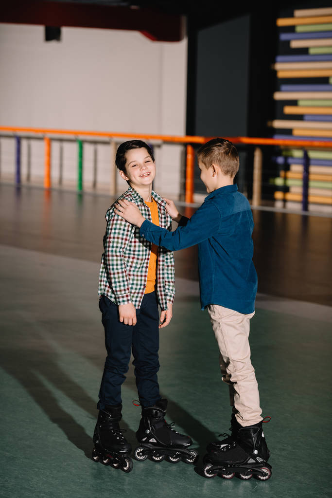  Pretty boy touching laughing friend while standing in spacious roller rink - Photo, Image