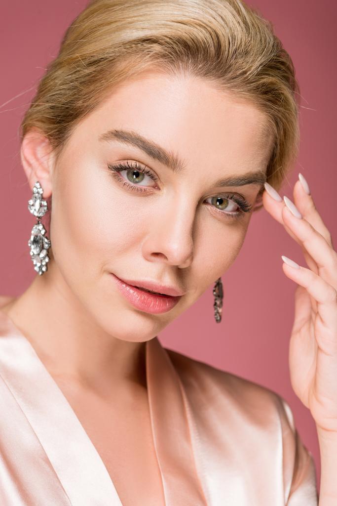 portrait of attractive blonde woman posing in earrings and silk robe, isolated on pink - Photo, Image