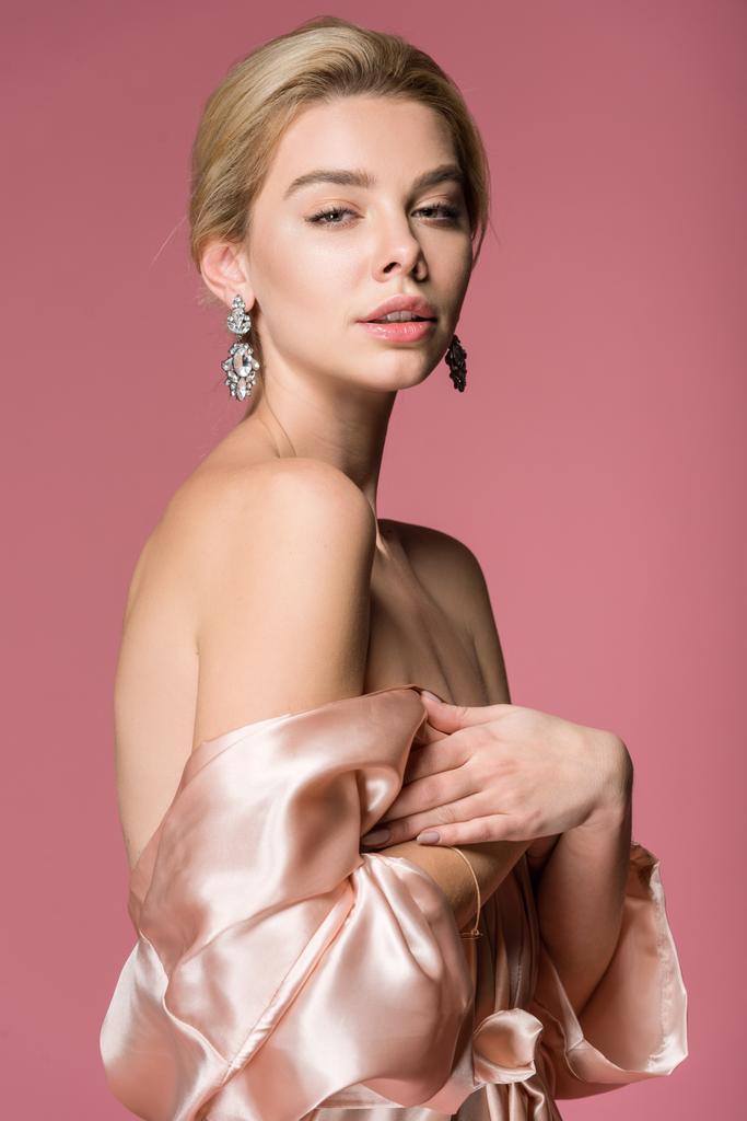 エレガントな金髪女性のイヤリングとピンクの分離、シルクのローブでポーズ - 写真・画像