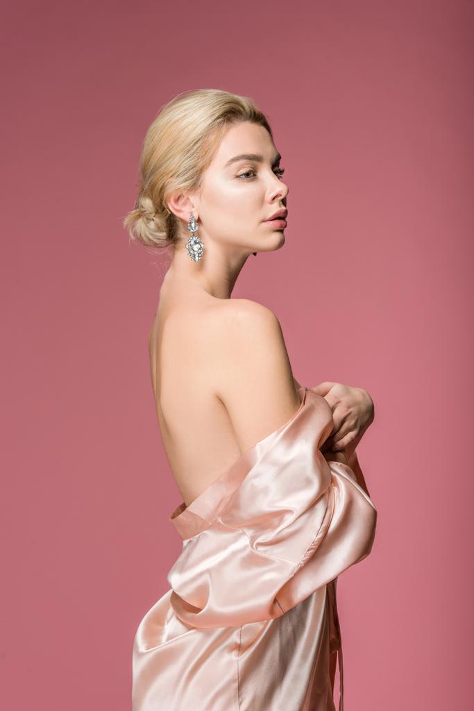 elegante chica elegante posando en pendientes y túnica de seda, aislado en rosa
 - Foto, imagen
