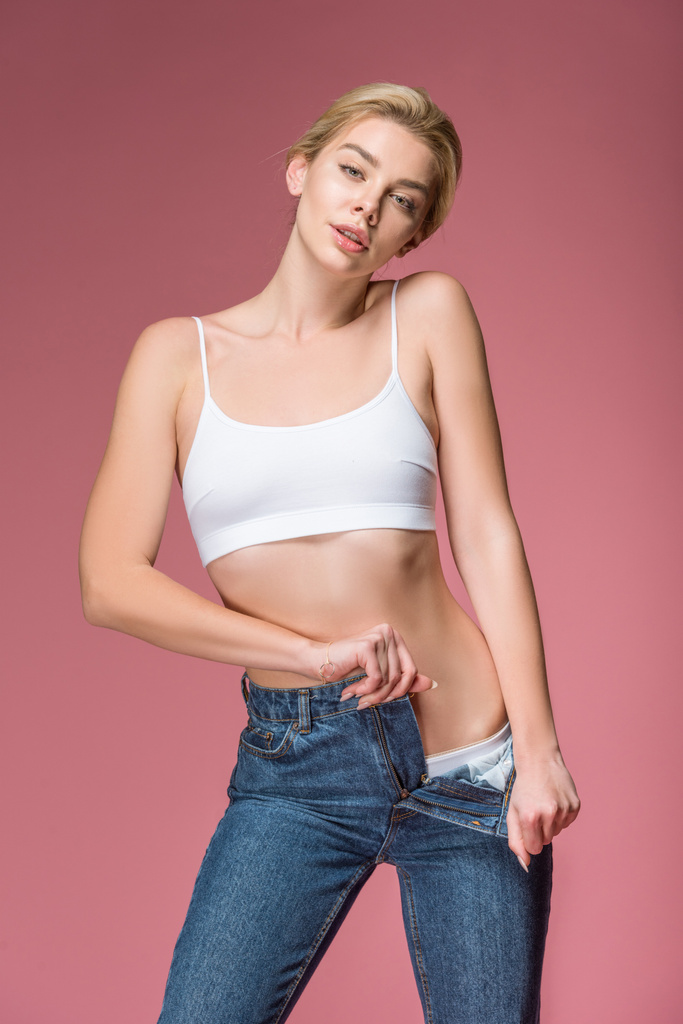 beautiful blonde woman posing in jeans and white bra, isolated on pink - Photo, Image