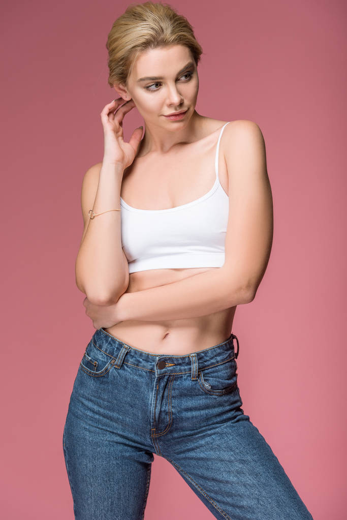 schöne blonde Frau posiert in Jeans und weißem BH, isoliert auf rosa - Foto, Bild
