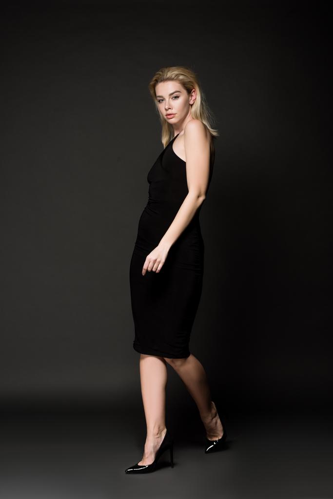 schöne junge Frau in elegantem schwarzen Kleid posiert auf schwarz - Foto, Bild