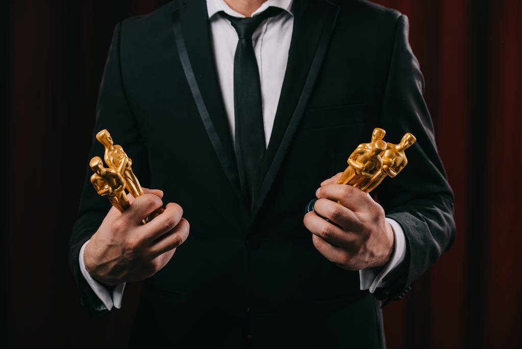 KYIV, UKRAINE - JANUARY 10, 2019: partial view of man in suit holding oscar awards on dark background - Photo, Image
