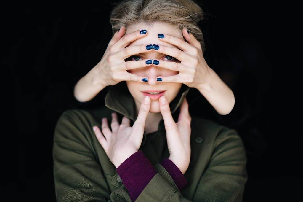 conceptuele portret van een jonge vrouw met handen op gezicht op zwarte achtergrond - Foto, afbeelding