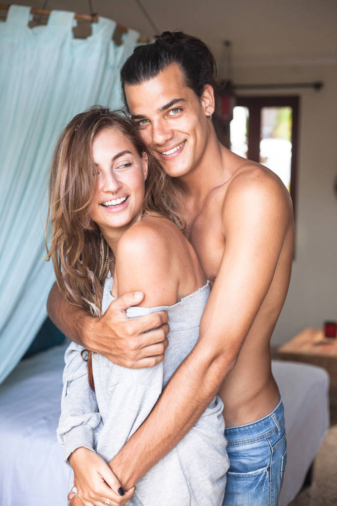 Jonge aantrekkelijke knappe Glimlachende man en vrouw knuffelen in de kamer. Meisje gekleed in een hoodie. man met een naakte torso - Foto, afbeelding