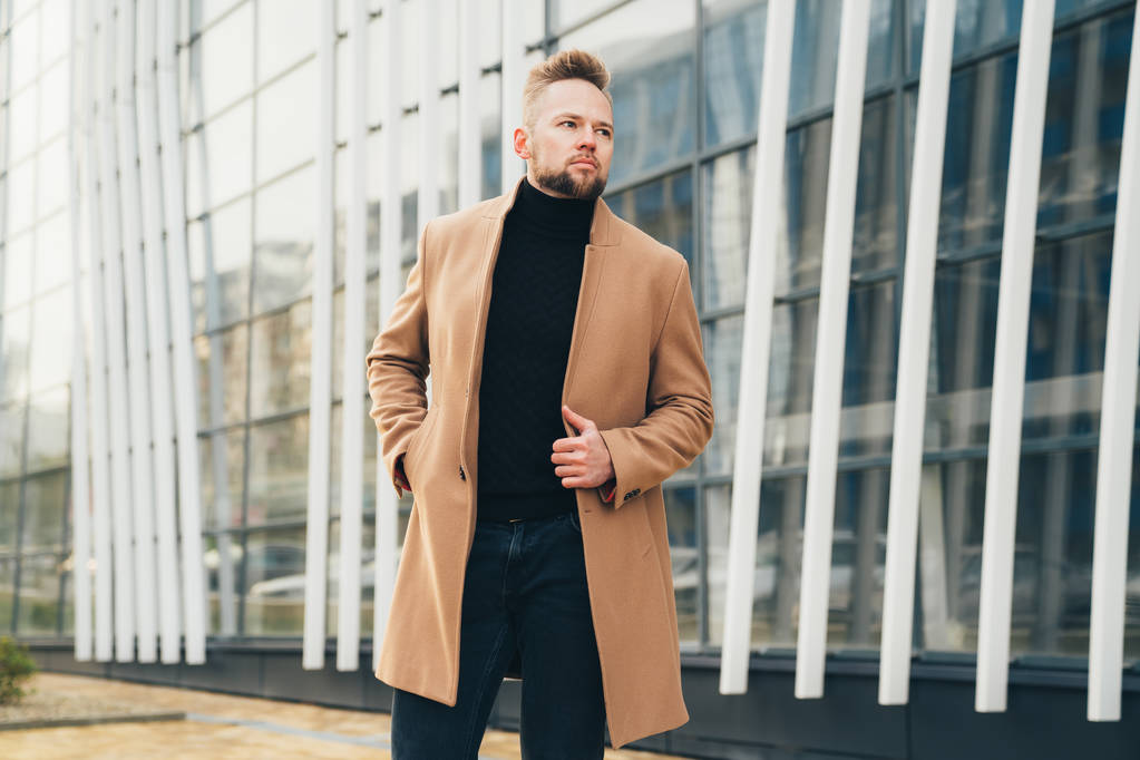 Úspěšný podnikatel v kabátě drží ruku v kapse a pózuje v moderní městské ulici - Fotografie, Obrázek
