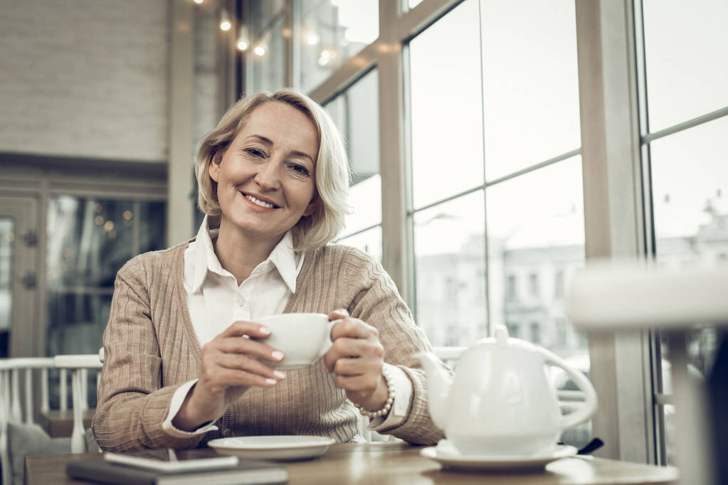 Elegante mujer madura con arrugas faciales bebiendo té en la cafetería
 - Foto, imagen