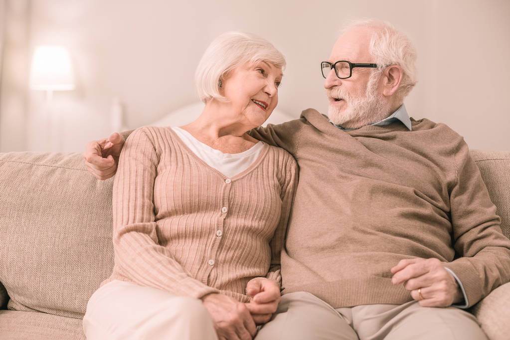 Entspannung zu Hause. Aufmerksamer bärtiger Rentner dreht Kopf, während er seiner Partnerin zuhört - Foto, Bild