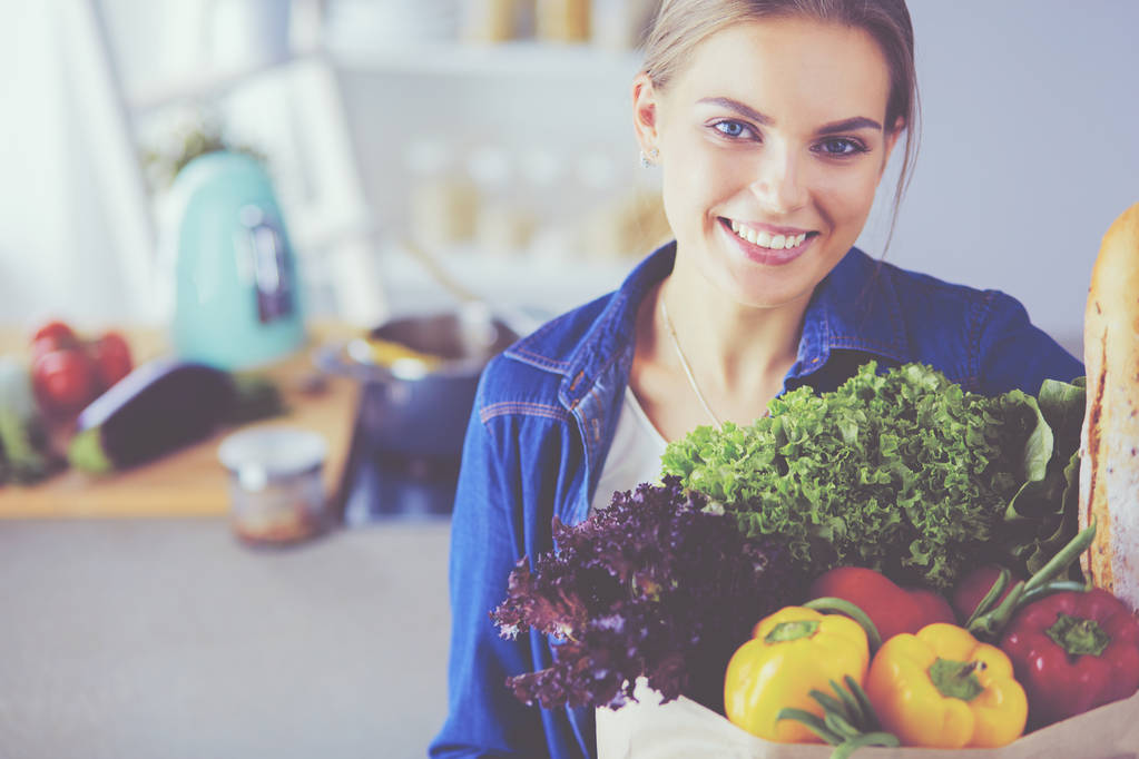 Mladá žena drží nákupní tašku s potravinami se zeleninou.Stojící v kuchyni - Fotografie, Obrázek