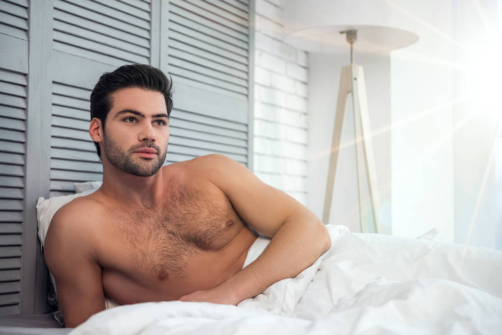 γυμνό άνδρα που βρίσκεται στο στο κρεβάτι και κοιτάζοντας μακριά το πρωί - Φωτογραφία, εικόνα