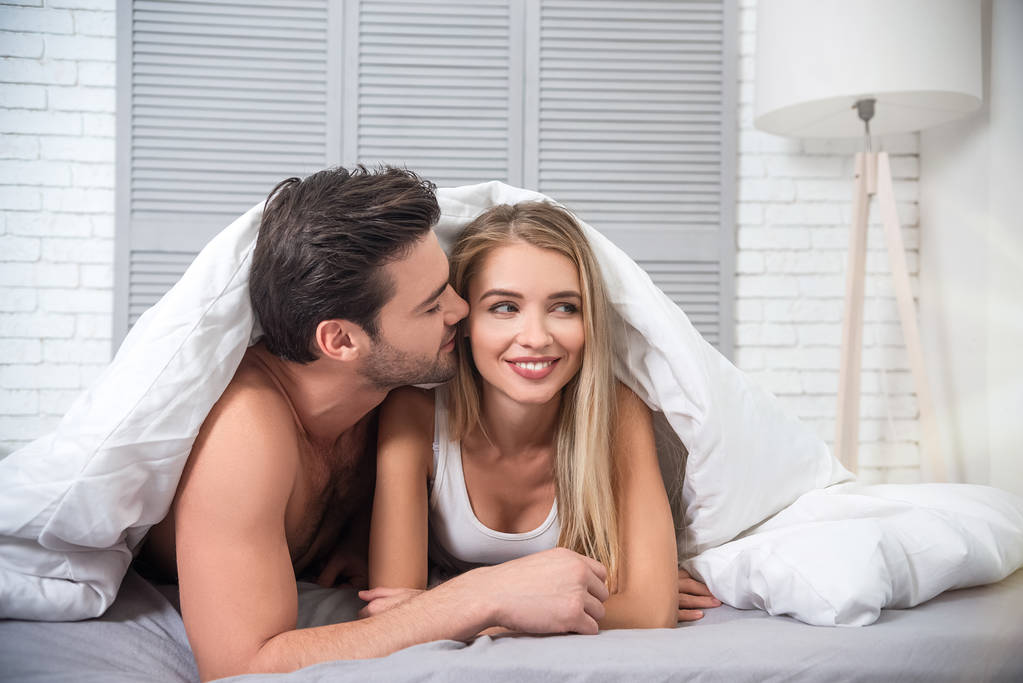 портрет пары, лежащей под одеялом на кровати дома
 - Фото, изображение