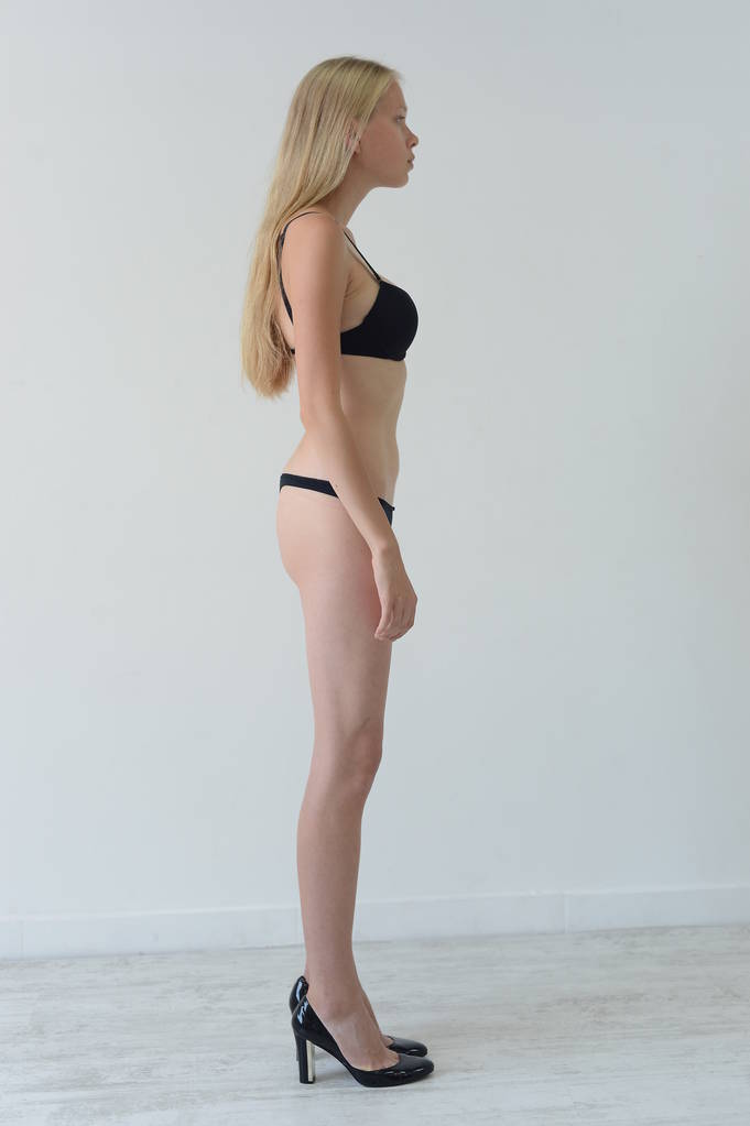 Model testet Mädchen in schwarzer Dessous mit Tätowierung posiert im Studio auf grauem Hintergrund - Foto, Bild