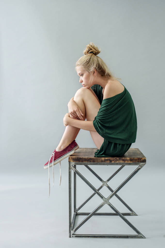Dziewczyna w zielonej piżamie jedwabiu z rozkładu pozowanie na krześle w Studio na szarym tle - Zdjęcie, obraz