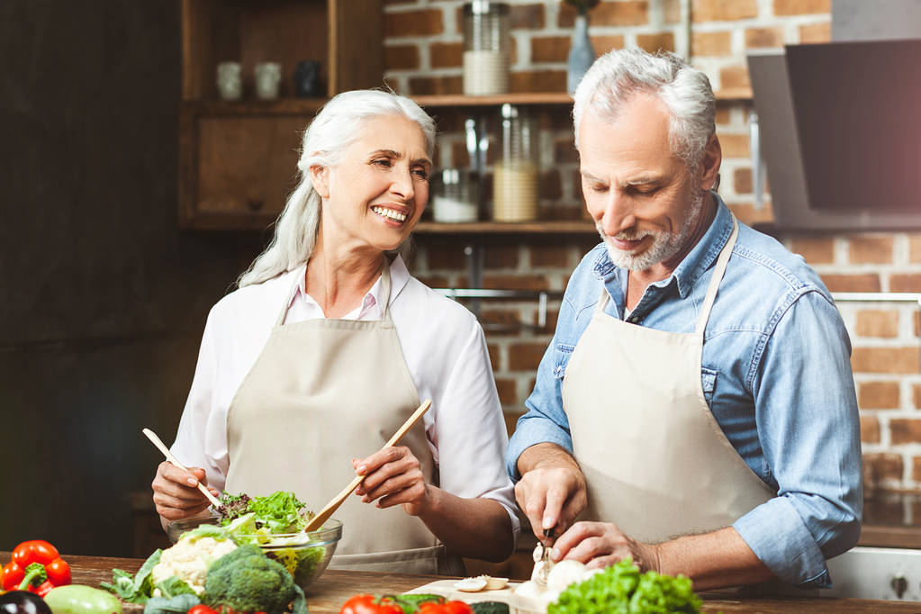 sorridente coppia di anziani taglio verdure per insalata in cucina
 - Foto, immagini