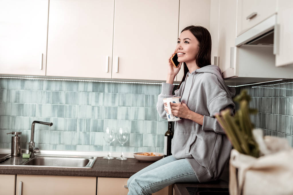 Dark-haired woman wearing oversize hoodie sitting near sink - Photo, Image