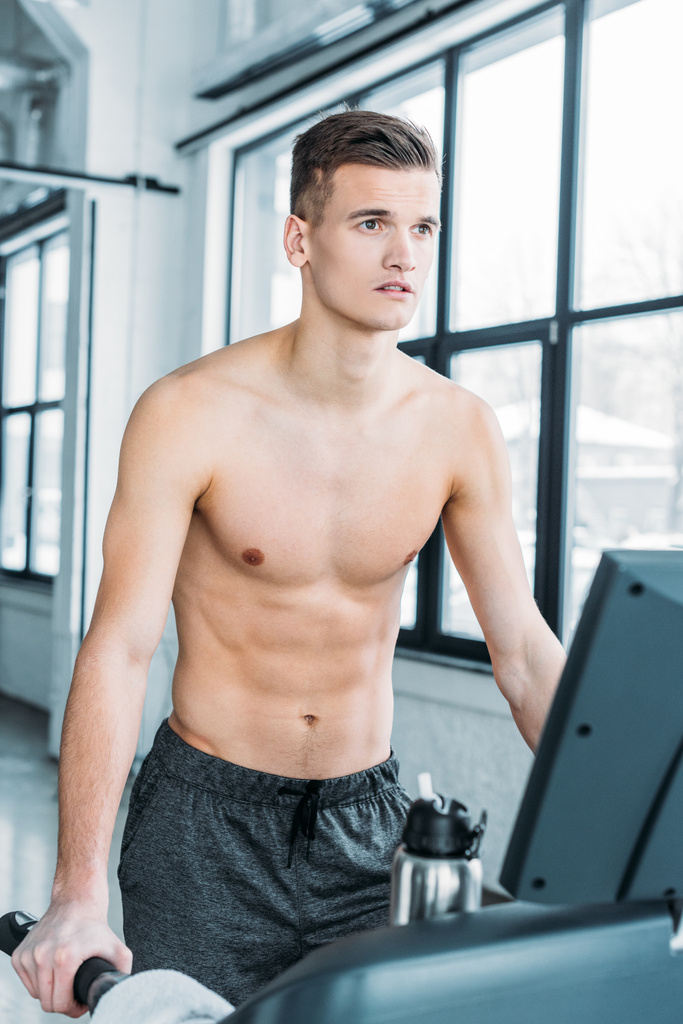 м'язистий без сорочки чоловік працює на біговій доріжці і дивиться в спортзал
 - Фото, зображення