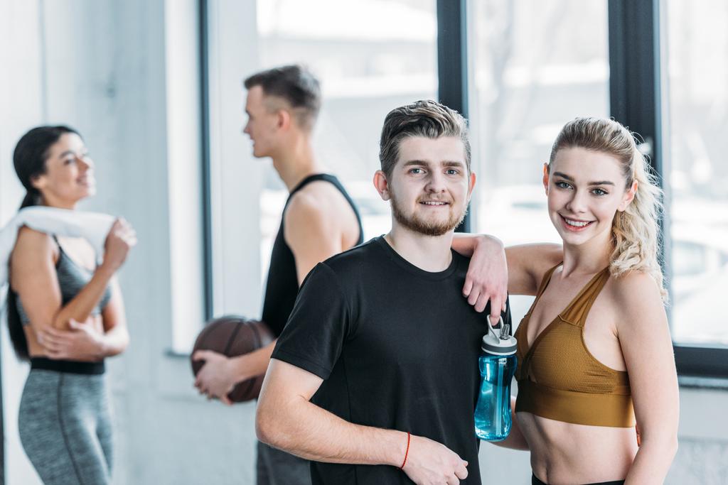 счастливый молодой человек и женщина в спортивной одежде стоят вместе и улыбаются перед камерой в тренажерном зале
 - Фото, изображение