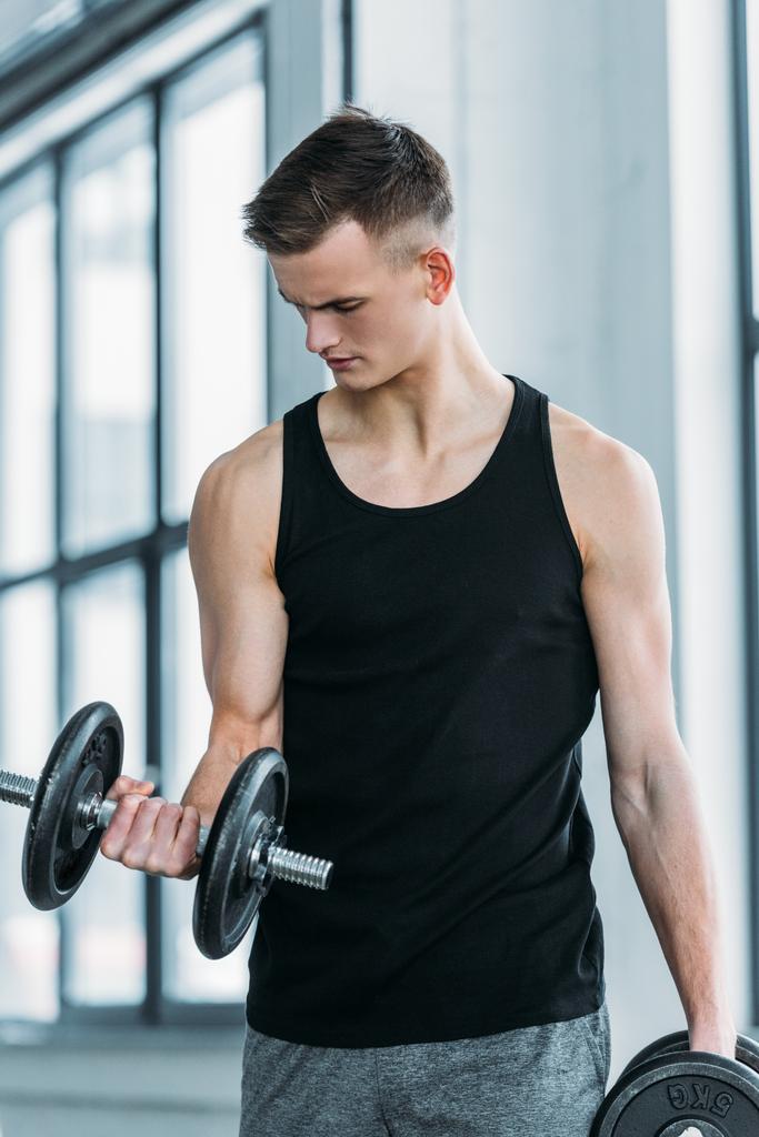handsome young sportsman exercising with dumbbells in gym - Photo, Image