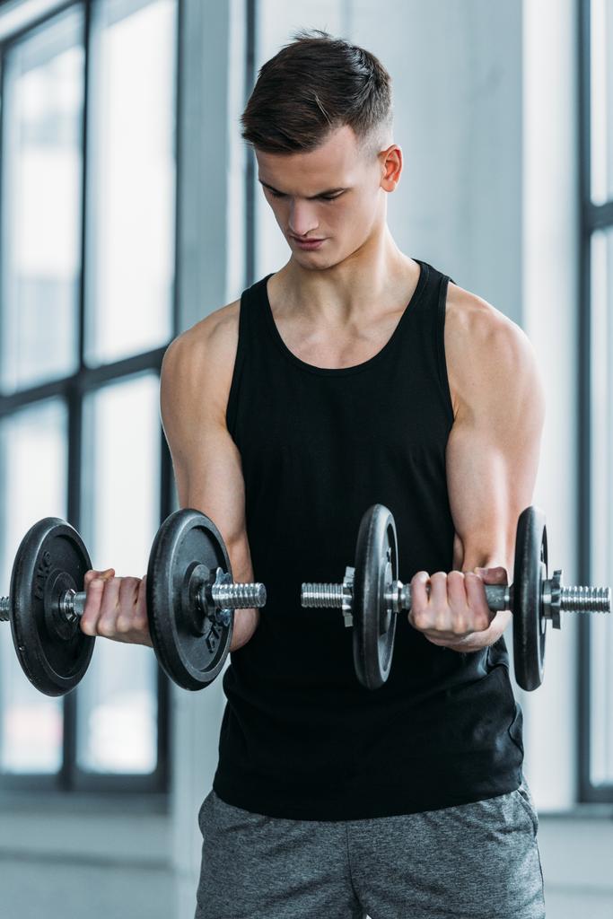 concentrated muscular man training with dumbbells in gym - Photo, Image