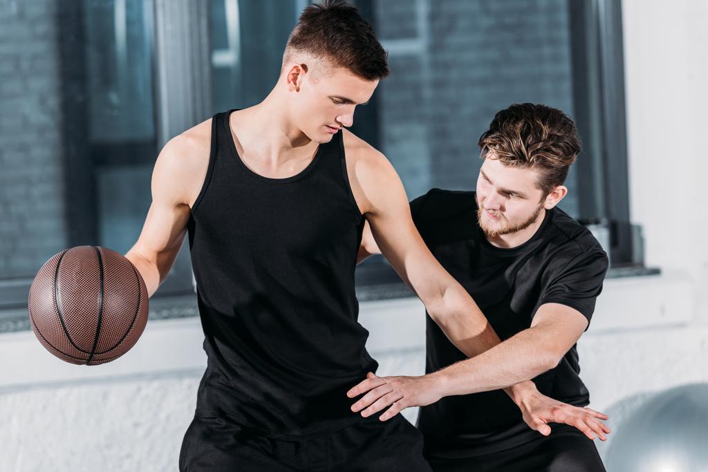 αθλητική νεαρούς άνδρες σε αθλητικά ρούχα, παίζοντας μπάσκετ, σε γυμναστήριο  - Φωτογραφία, εικόνα