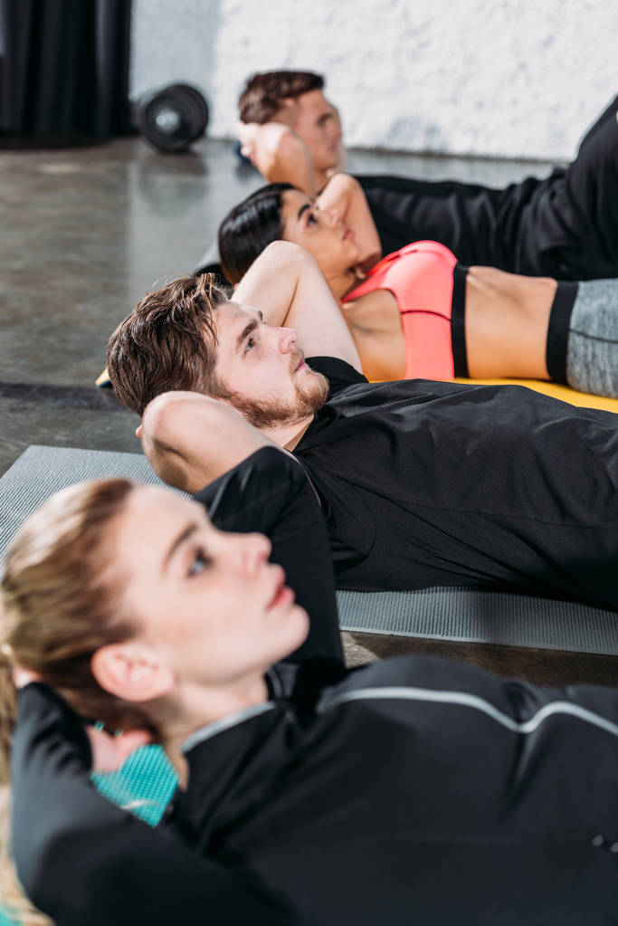 σπορ πολυφυλετικής νέους ξαπλωμένος σε χαλάκια γιόγκα και κάνει abs στο γυμναστήριο - Φωτογραφία, εικόνα