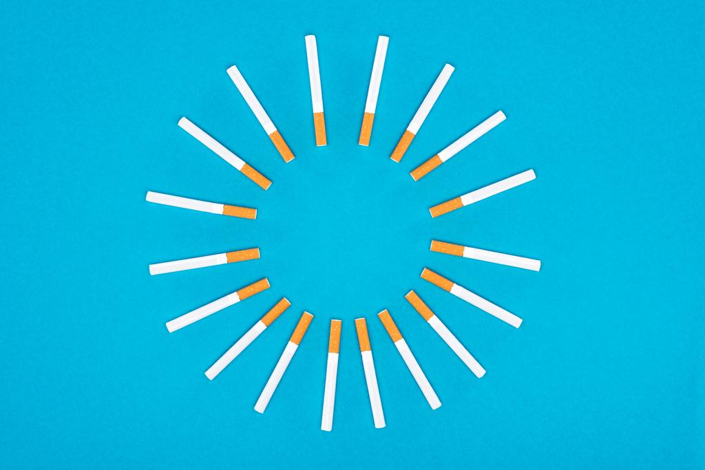 Vlakke leggen met sigaretten liggen in cirkel geïsoleerd op blauw  - Foto, afbeelding