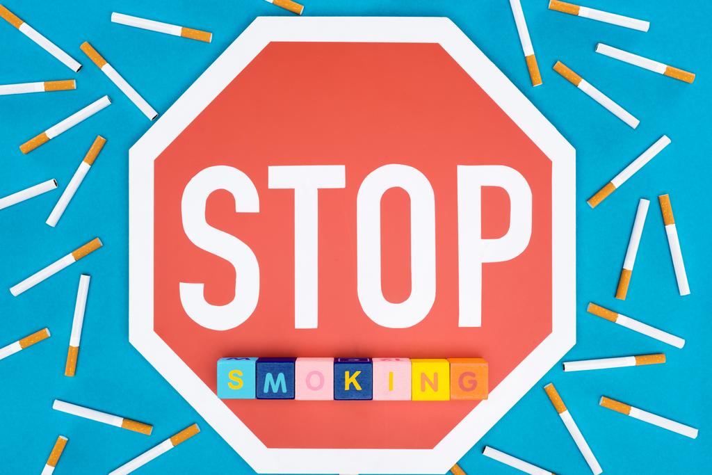 Top view of stop sign, cigarettes and blocks with letters isolated on blue, stop smoking concept - Photo, Image