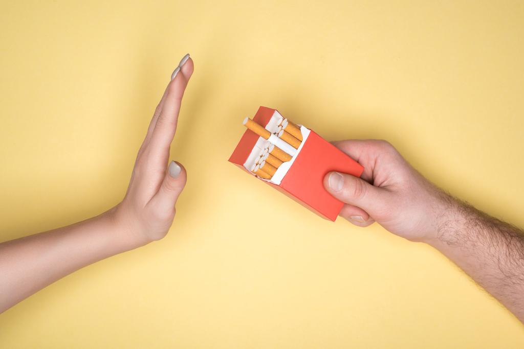 abgeschnittene Ansicht der jungen Frau verweigert Zigaretten isoliert auf gelb, Rauchen aufhören Konzept - Foto, Bild