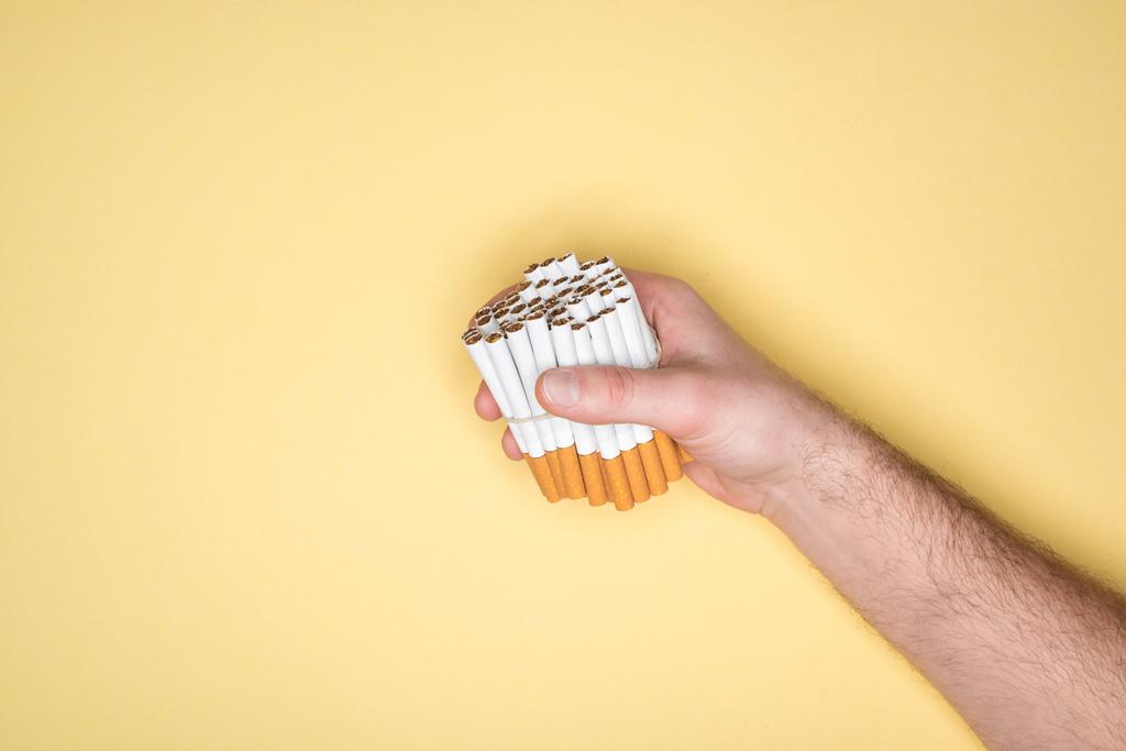 Gedeeltelijke weergave van man met sigaretten in de vuist geïsoleerd op geel - Foto, afbeelding