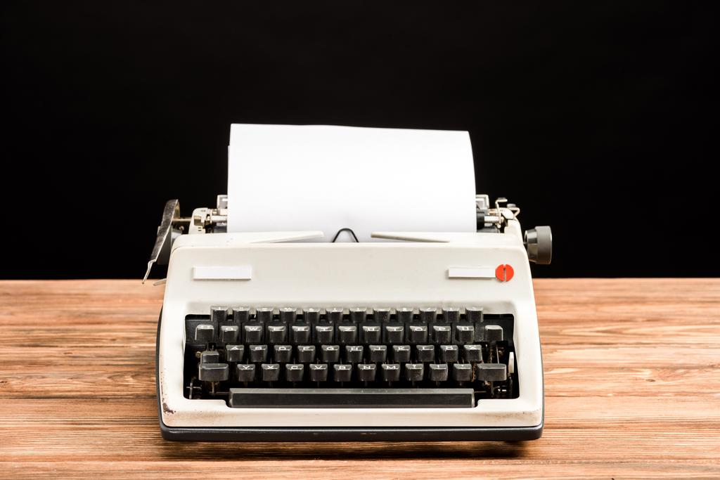 Vintage-Schreibmaschine mit Papier auf Holztisch isoliert auf schwarz - Foto, Bild