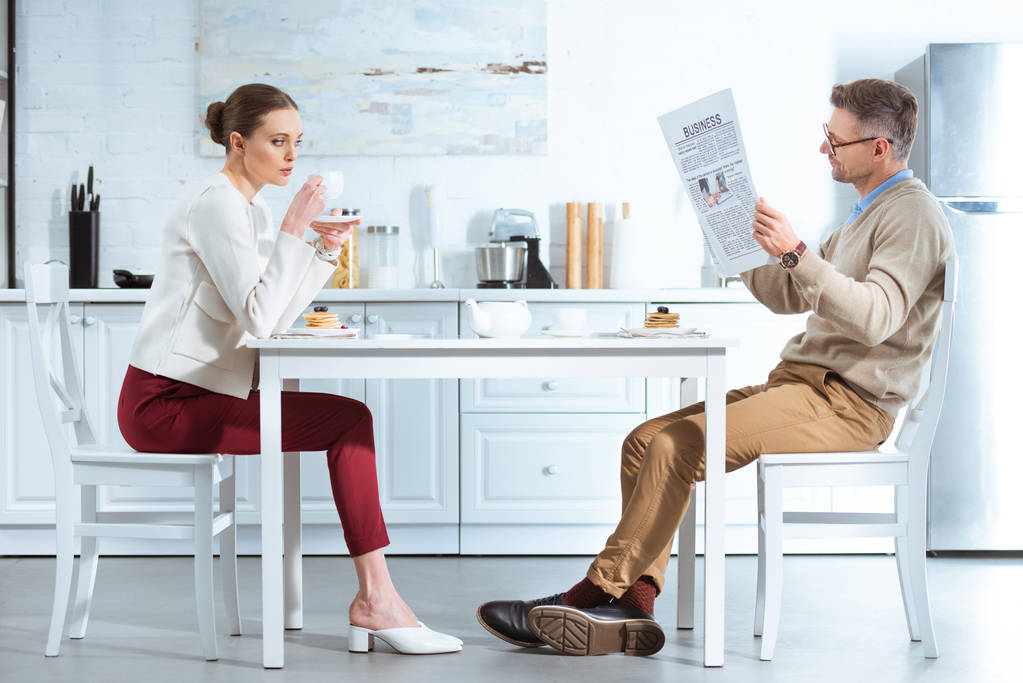 donna insoddisfatta che beve tè mentre l'uomo legge il giornale aziendale durante la colazione in cucina
 - Foto, immagini